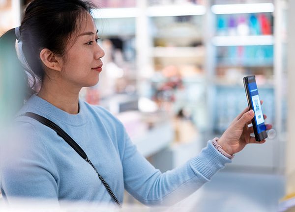 Eine Person h&auml;lt ihr Smartphone mit Payback Pay in Richtung einer Kasse.
