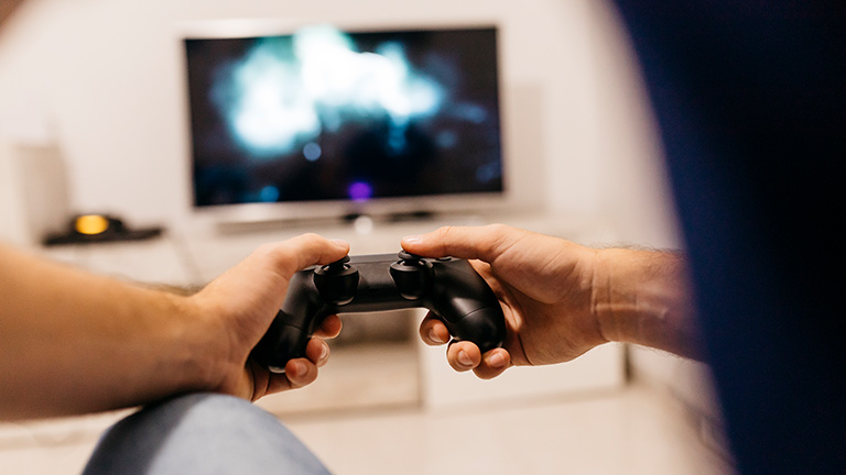 Eine Person hält einen PS4-Controller in der Hand und spielt etwas.