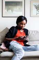 Eine Person sitzt auf dem Sofa und schaut auf ihr Smartphone.