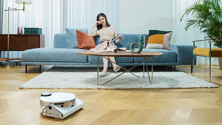 Der JetBot 90 AI+ fährt durch ein Wohnzimmer. Im Hintergrund sitzt eine Person auf einem Sofa.