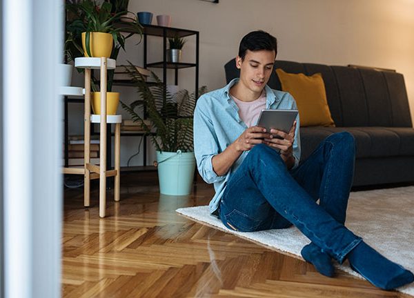 Eine Person sitzt auf einem Teppich und h&auml;lt ein Tablet in der Hand.