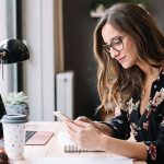 Eine Person sitzt an einem Schreibtisch und h&auml;lt ein Smartphone in der Hand.