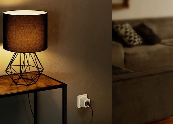 Ein Apple HomePod Mini auf einem Tisch. Daneben steht eine Lampe, die &uuml;ber eine Eve Energy mit dem Strom verbunden ist.
