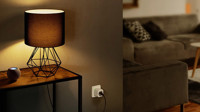 Ein Apple HomePod Mini auf einem Tisch. Daneben steht eine Lampe, die &uuml;ber eine Eve Energy mit dem Strom verbunden ist.