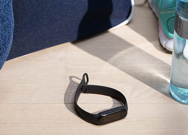 Das Fitness-Armband Mi Smart Band 5 von Xiaomi liegt auf einem hellen Holztisch. Ringsherum befinden sich Sportutensilien.