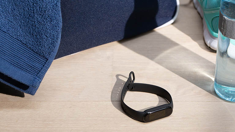 Das Fitness-Armband Mi Smart Band 5 von Xiaomi liegt auf einem hellen Holztisch. Ringsherum befinden sich Sportutensilien.
