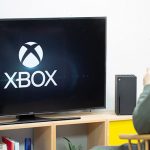 Eine Person sitzt vor einer Xbox Series X. Auf dem Fernseher ist der Startbildschirm zu sehen.