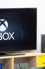 Eine Person sitzt vor einer Xbox Series X. Auf dem Fernseher ist der Startbildschirm zu sehen.