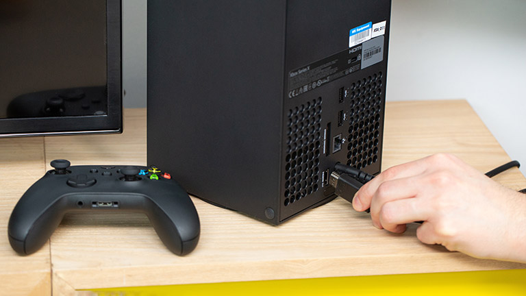 Eine Person steckt ein HDMI-Kabel in den Port hinten an der Xbox Series X.