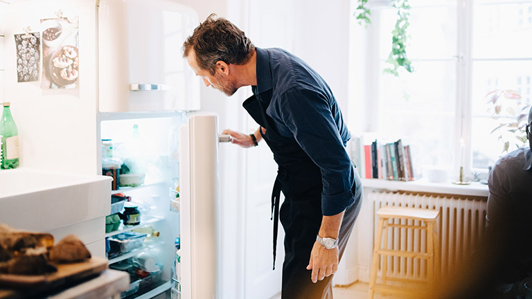 Ein Mann öffnet einen Kühlschrank und schaut hinein.