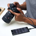 Eine Person h&auml;lt die Sony Alpha 1, die gerade Bilder per Kabel an ein Smartphone &uuml;bertr&auml;gt.