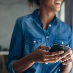 Eine Person h&auml;lt ein Android-Smartphone in der Hand und l&auml;chelt dabei in die Ferne.