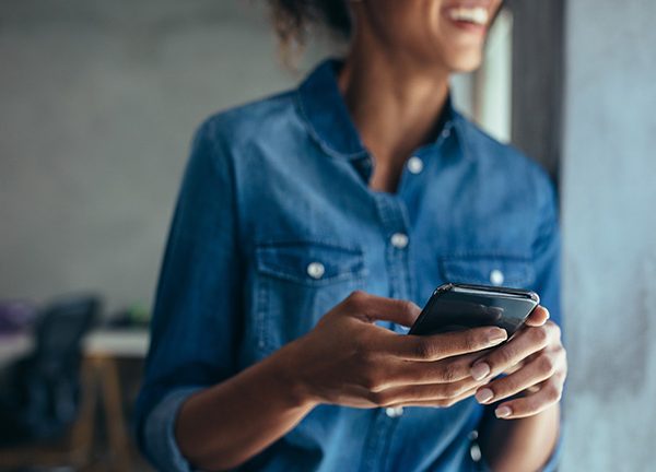 Eine Person h&auml;lt ein Android-Smartphone in der Hand und l&auml;chelt dabei in die Ferne.