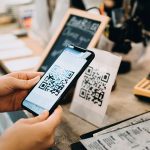 Eine Person h&auml;lt ihr Smartphone auf einen QR-Code, um ihn mit der Kamera auszulesen.