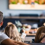 Eine Familie mit zwei Kindern sitzt vor dem Fernseher und schaut sich einen Film an.