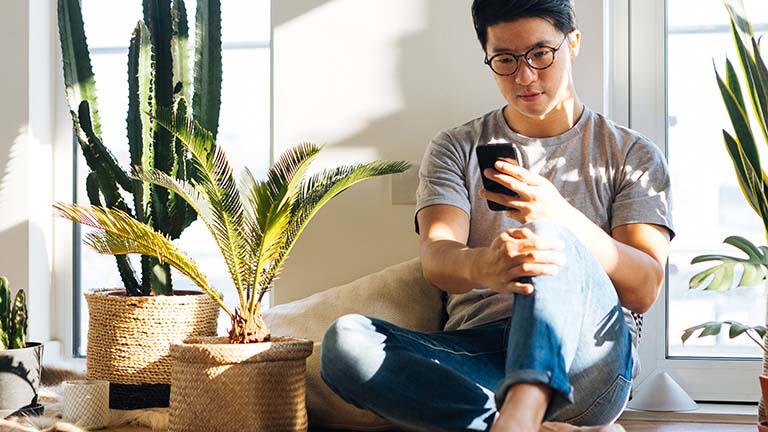 Eine Person sitzt auf einer Fensterbank und schaut auf ihr Smartphone.