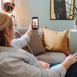 Eine Person sitzt auf dem Sofa und telefoniert per Videoübertragung mit einer anderen Person.