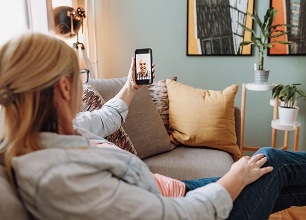 Eine Person sitzt auf dem Sofa und telefoniert per Video&uuml;bertragung mit einer anderen Person.
