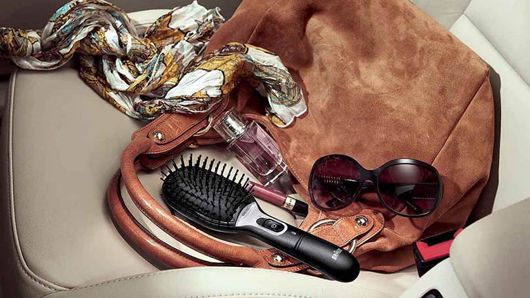 Die Satin Hair 7 Haarbürste von Braun liegt auf dem Beifahrersitz eines Autos neben einer Handtasche.