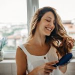 Eine Person steht im Badezimmer und b&uuml;rstet sich die langen Haare.