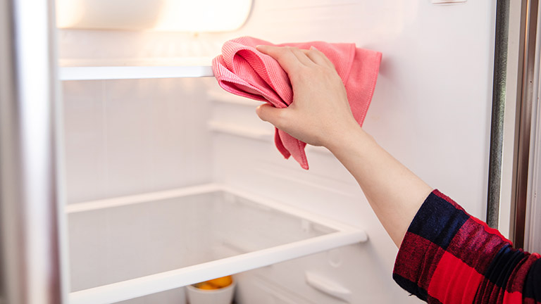 Eine Person reinigt den Innenraum eines Kühlschranks mit einem Tuch.