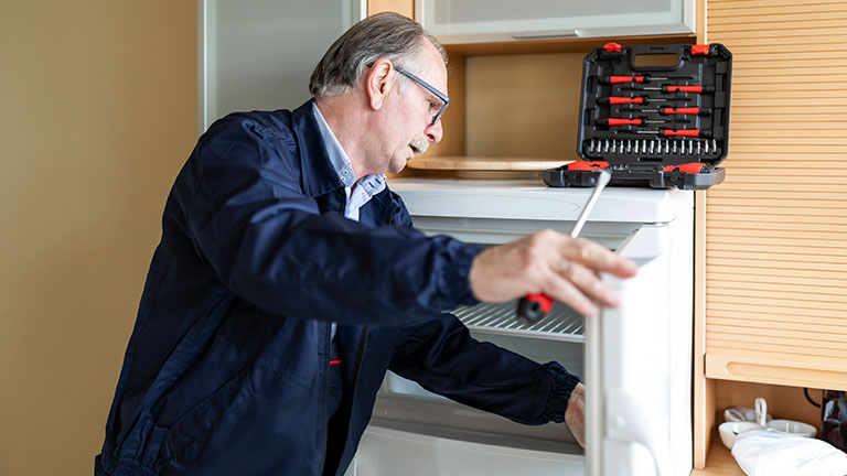 Ein Handwerker hält einen Schraubendreher in der Hand und begutachtet die Tür eines Kühlschranks.