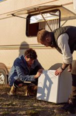 Kühlschrank für Wohnmobil & Auto Zwei Personen beugen sich über einen Kühlschrank vor einem Wohnwagen.