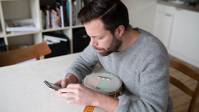 Eine Person sitzt an einem Tisch mit einem Banjo und schaut auf ihr Handy.