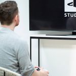 Eine Person sitzt vor einem Fernseher. Darunter steht eine PlayStation 5.