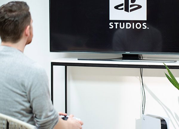 Eine Person sitzt vor einem Fernseher. Darunter steht eine PlayStation 5.