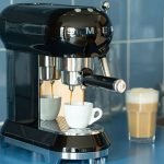 Eine Espressomaschine im Retro-Look der Marke Smeg steht auf einer K&uuml;chenzeile und bereitet einen Espresso zu.