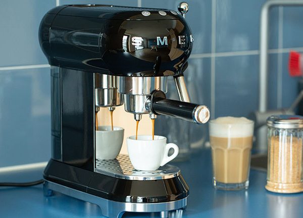 Eine Espressomaschine im Retro-Look der Marke Smeg steht auf einer Küchenzeile und bereitet einen Espresso zu.
