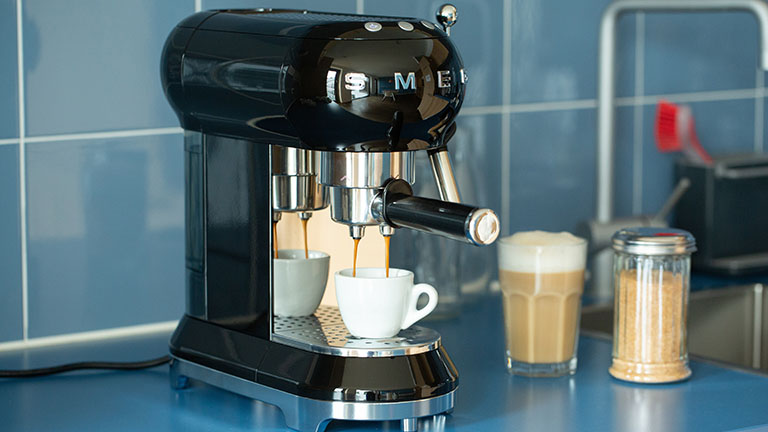 Eine Espressomaschine im Retro-Look der Marke Smeg steht auf einer K&uuml;chenzeile und bereitet einen Espresso zu.