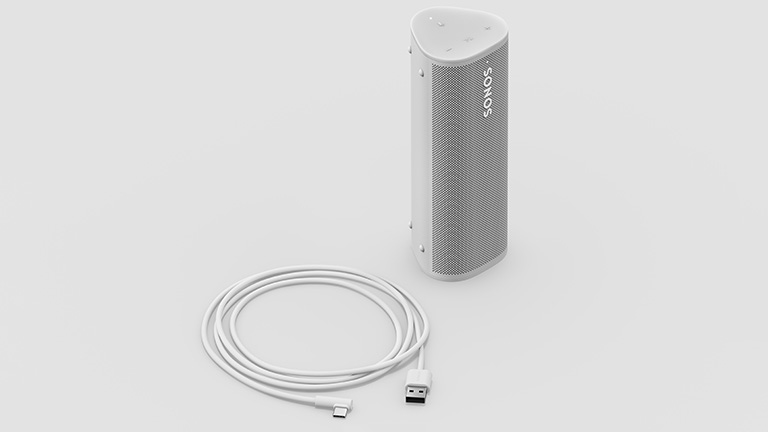 Der Sonos Roam in weiß in aufrechter Position, daneben liegt das der Packung beiliegende Ladekabel.