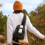 Ein Mann streift durch ein Feld. An seinem Rucksack h&auml;ngt der Bluetooth-Lautsprecher Sonos Roam in wei&szlig;.