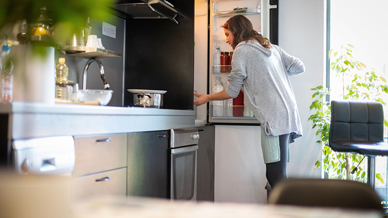 Eine Person &ouml;ffnet den K&uuml;hlschrank und schaut hinein.