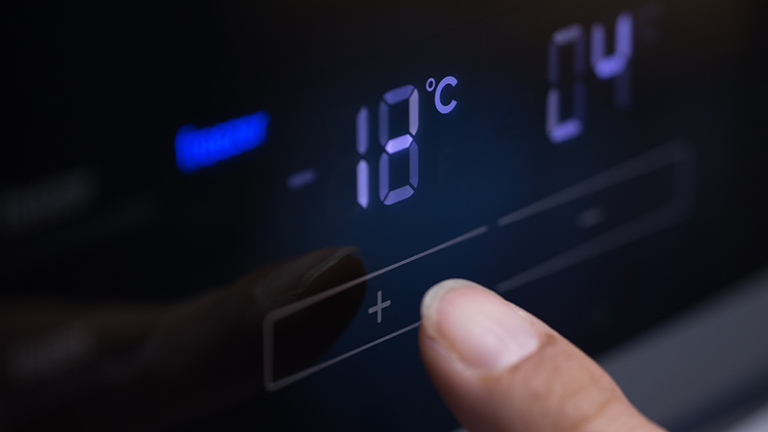 Eine Person stellt an einem Kühlschrank -18 Grad für den Gefrierteil ein.
