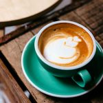 Foto einer Tasse gef&uuml;llt mit Kaffee, auf dem mit Milchschaum eine Blume angedeutet ist.