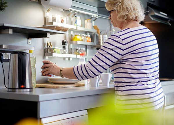 Eine Person steht in der K&uuml;che, auf der Arbeitsplatte steht ein eingeschalteter Wasserkocher.