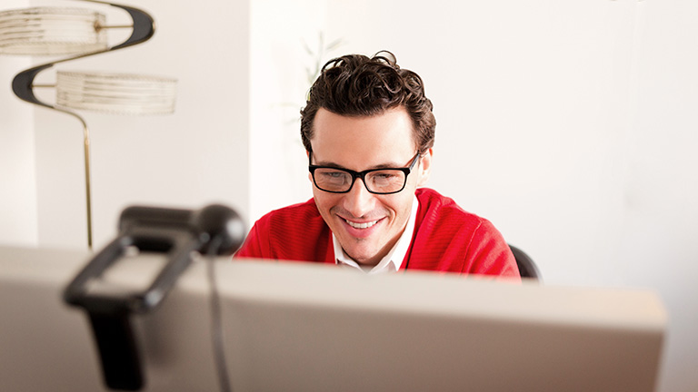 Eine Person sitzt vor einer Webcam und lächelt in Richtung des Bildschirms.