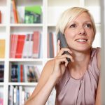 Eine Person sitzt an einem Schreibtisch und telefoniert mit einem Festnetztelefon.