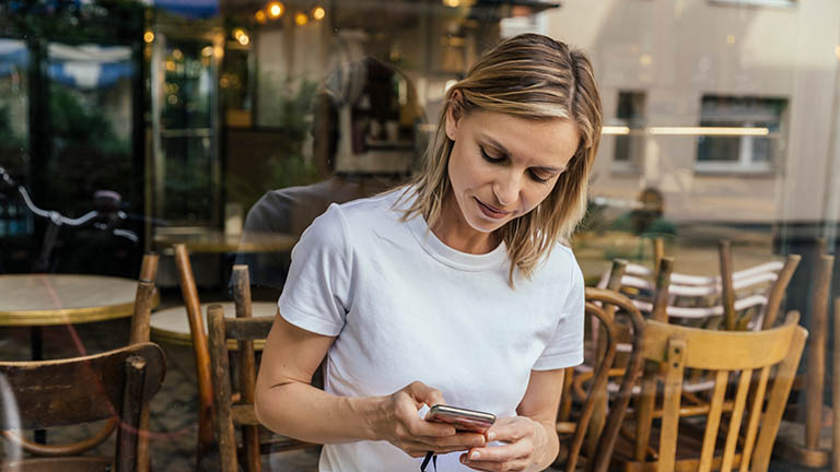 Eine Person steht vor einem Restaurant und hält ein Smartphone in der Hand.