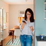 Eine Person steht an eine Wand gelehnt und h&auml;lt ihr Smartphone in der Hand.