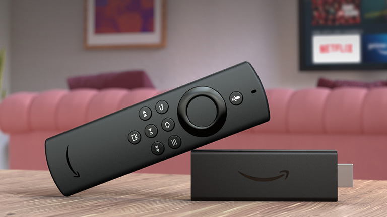 Produktfoto eines Amazon Fire TV Sticks vor einer Couch und einem Fernseher.