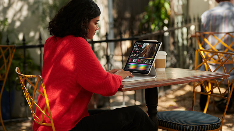 Eine Person sitzt an einem Kaffeetisch und bedient ihr iPad Pro über das Magic Keyboard.