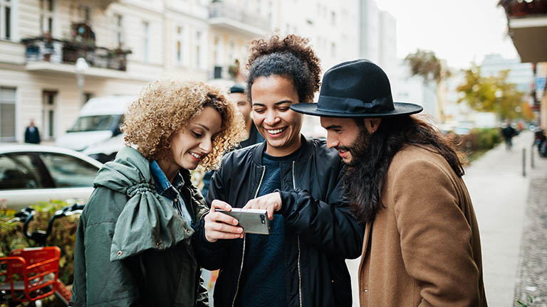 Drei Personen schauen zusammen auf ein Smartphone-Display und sind erfreut.