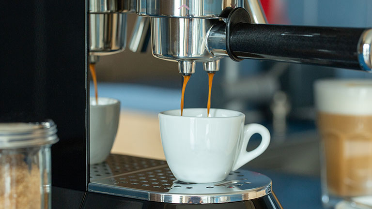 Aus dem Siebträger einer Smeg-Espressomaschine fließt frischer Kaffee in eine Tasse.