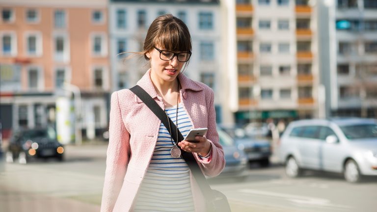 Eine Person geht durch die Stadt und schaut dabei auf ihr Smartphone.