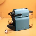 Die Nespresso Inissia auf einem Tisch. Vor der Maschine liegt eine Kapsel.