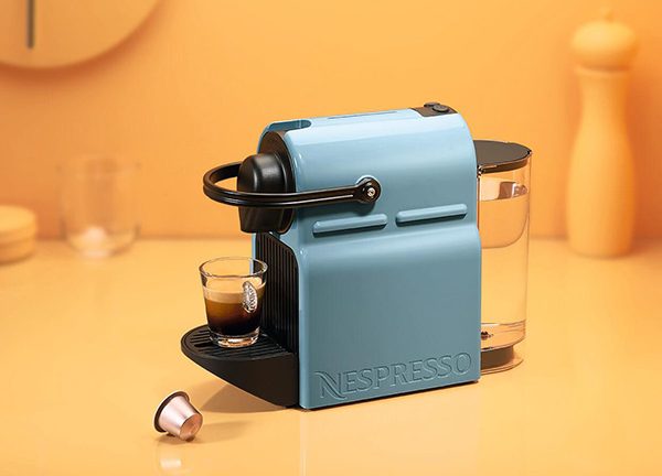 Die Nespresso Inissia auf einem Tisch. Vor der Maschine liegt eine Kapsel.